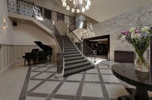 Uma escadaria imponente com um piano, uma mesa redonda com um vaso de flores e uma parede de pedra.