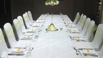 A long conference table with white tablecloths, chairs with white sashes, and a chandelier.
