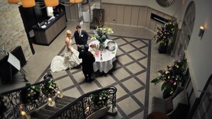 A wedding reception with a couple seated at a round table, surrounded by floral arrangements and a checkered floor. - Dumfries Arms Hotel (Cumnock)