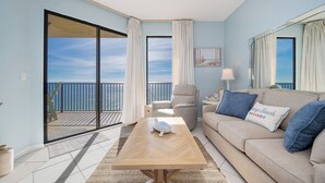 Una sala de estar con sofá, mesa de centro, silla y vista al mar a través de un ventanal corredero.