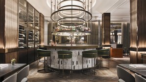 A bar area with a circular bar, green bar stools, and a wine display.