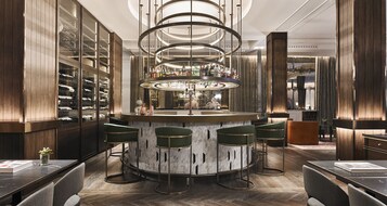 Un espace bar doté d’un comptoir circulaire, de tabourets de bar verts et d’un présentoir à vins.