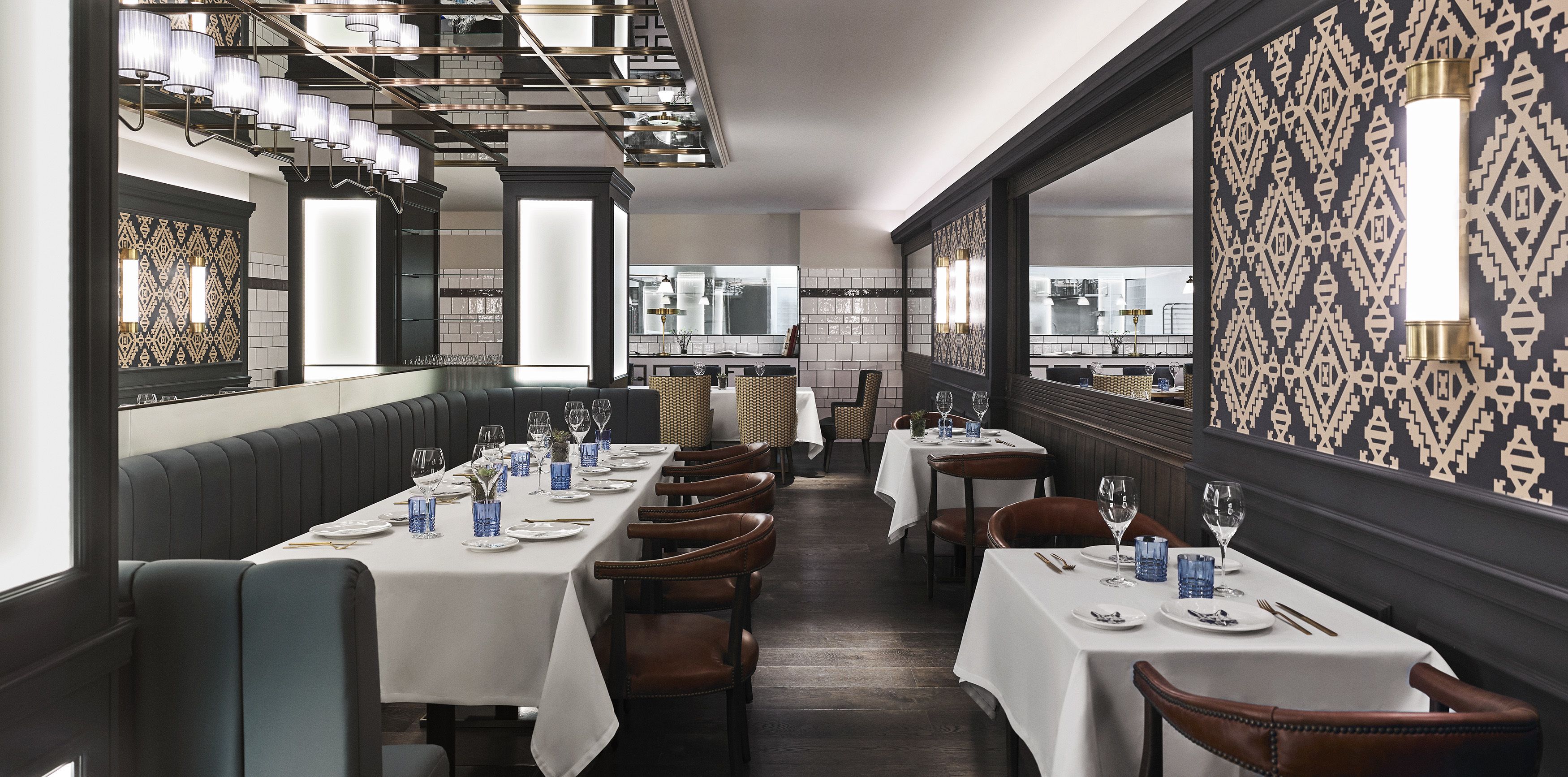 A restaurant with long tables, chairs, and a patterned wall.