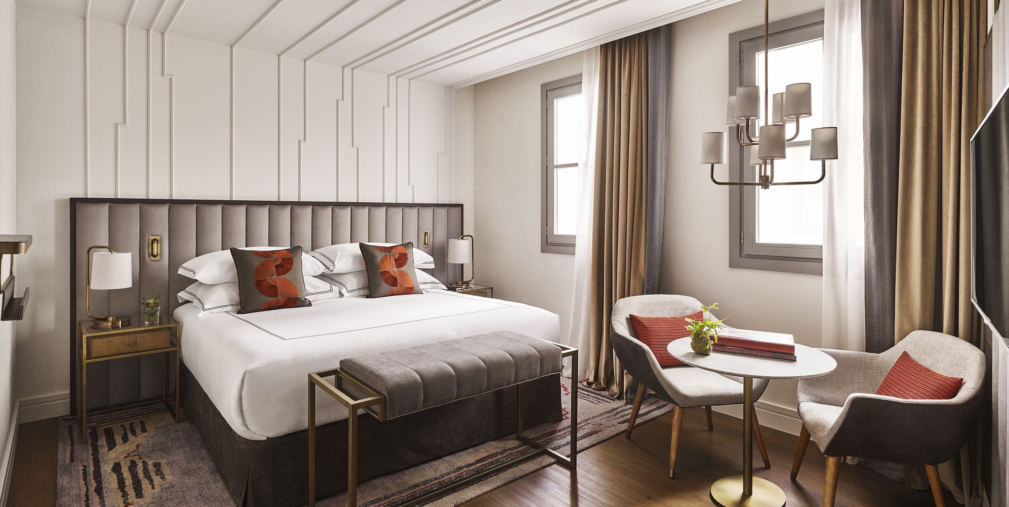 A hotel room with a large bed, bedside tables, a desk, a chair, and a window with curtains.