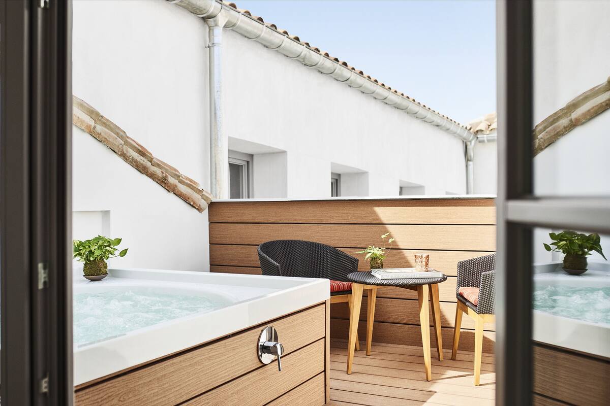 Un balcón con jacuzzi, sillas de mimbre y suelo de madera.
