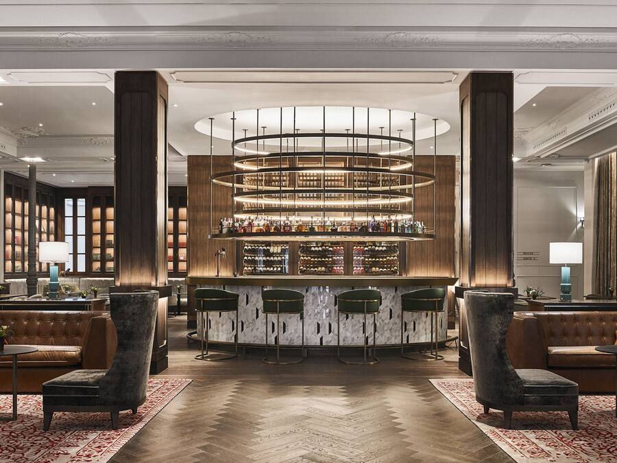 Un lobby espacioso con bar central, techos altos y muebles clásicos.
