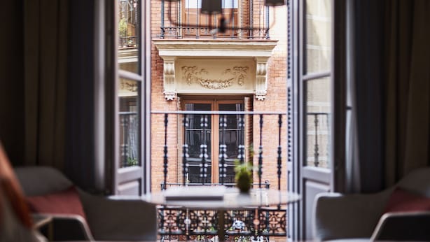 A view from a balcony with a table and chairs, a decorative iron railing, and a building facade with a balcony and windows.