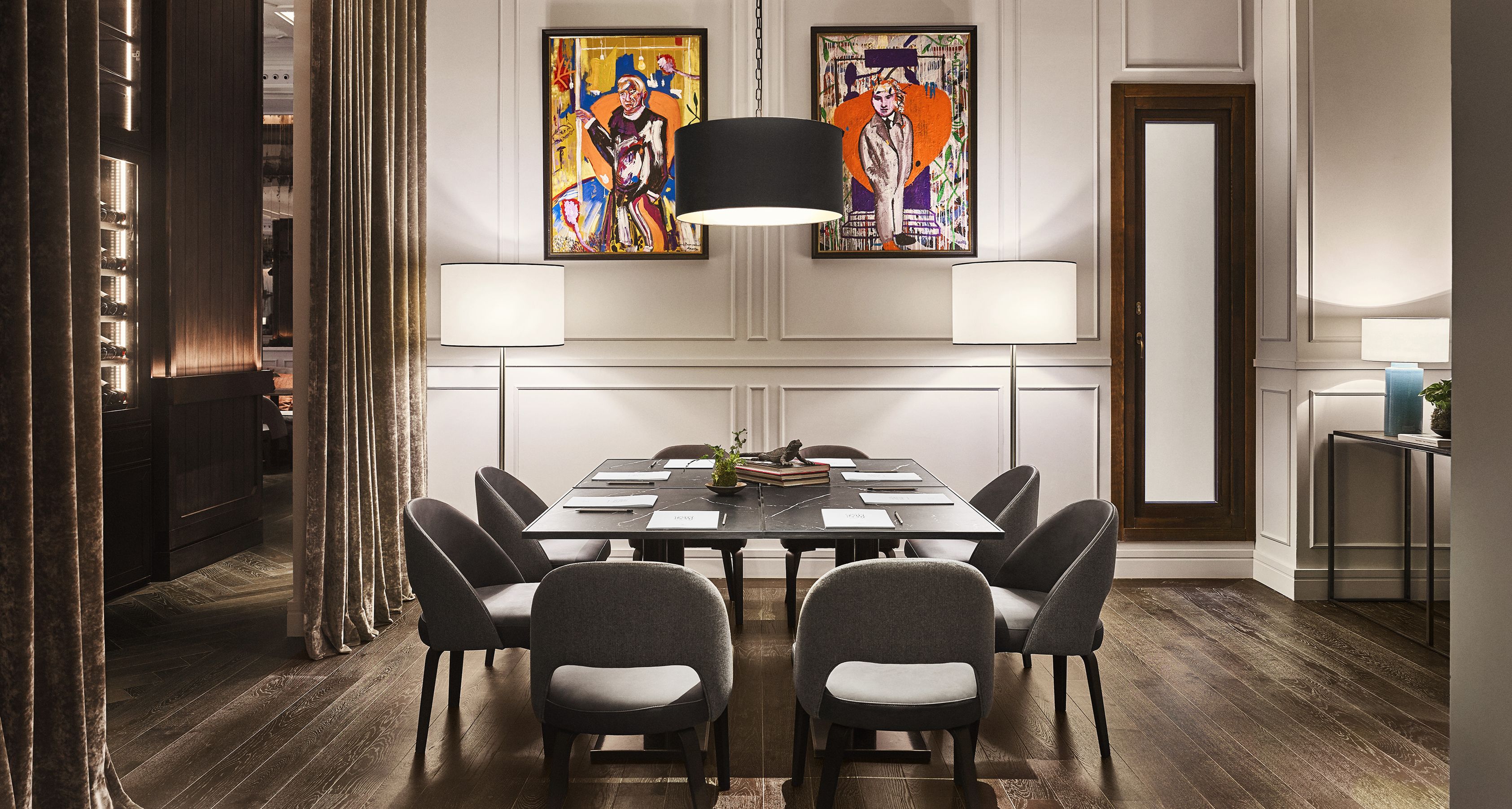 Un comedor moderno con una mesa de madera oscura, sillas tapizadas de gris y dos lámparas fijadas a la pared.