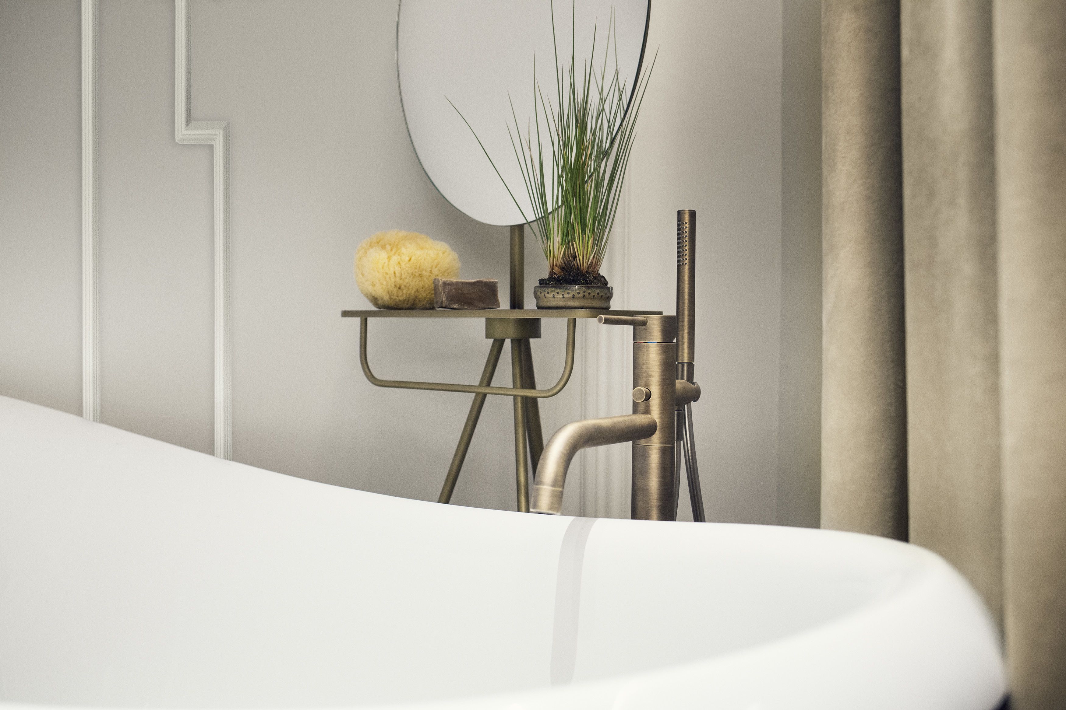A modern bathroom with a white bathtub, a small table with a potted plant, and a wall-mounted mirror.