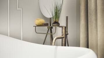A modern bathroom with a white bathtub, a small table with a potted plant, and a wall-mounted mirror.