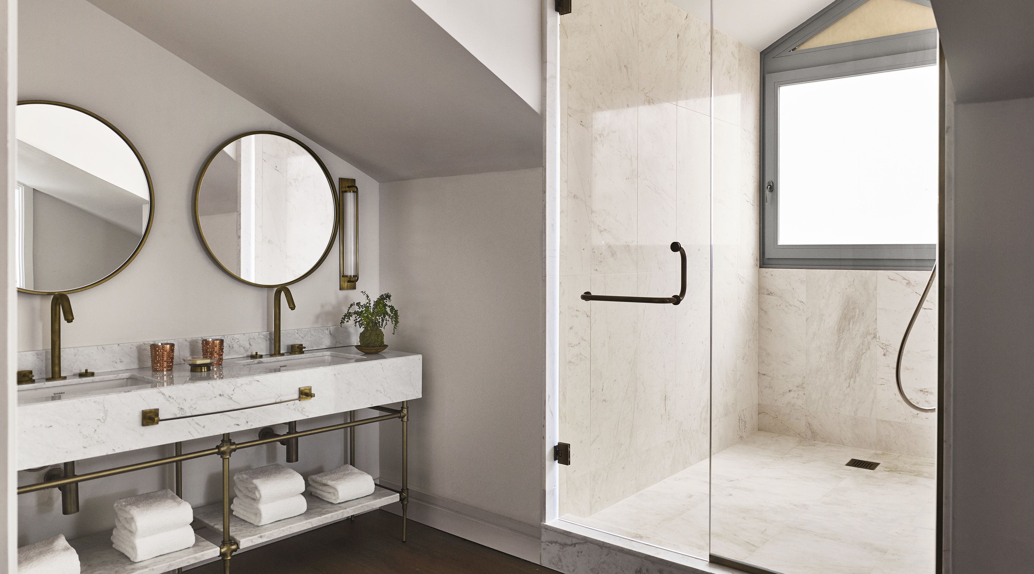 Une salle de bain moderne avec une douche à parois de verre, un meuble-lavabo en marbre avec des accessoires dorés et deux miroirs.