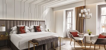 Une chambre d’hôtel moderne dotée d’un grand lit, de tables de chevet, d’un coin salon avec une table et des chaises, et d’un lustre.