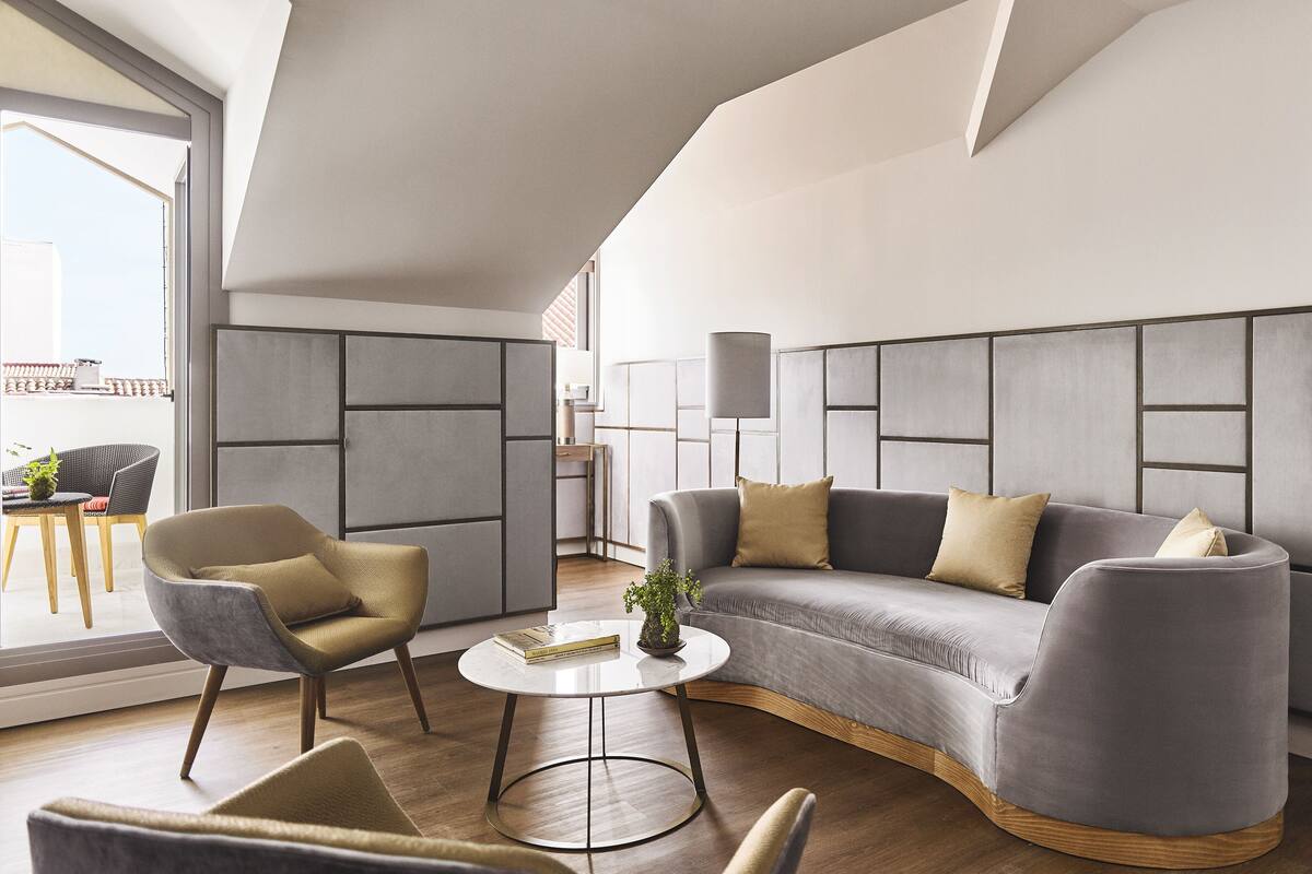 Una sala de estar moderna con un sofá gris curvo, dos sillones, una pequeña mesa redonda de centro y una lámpara de pie.