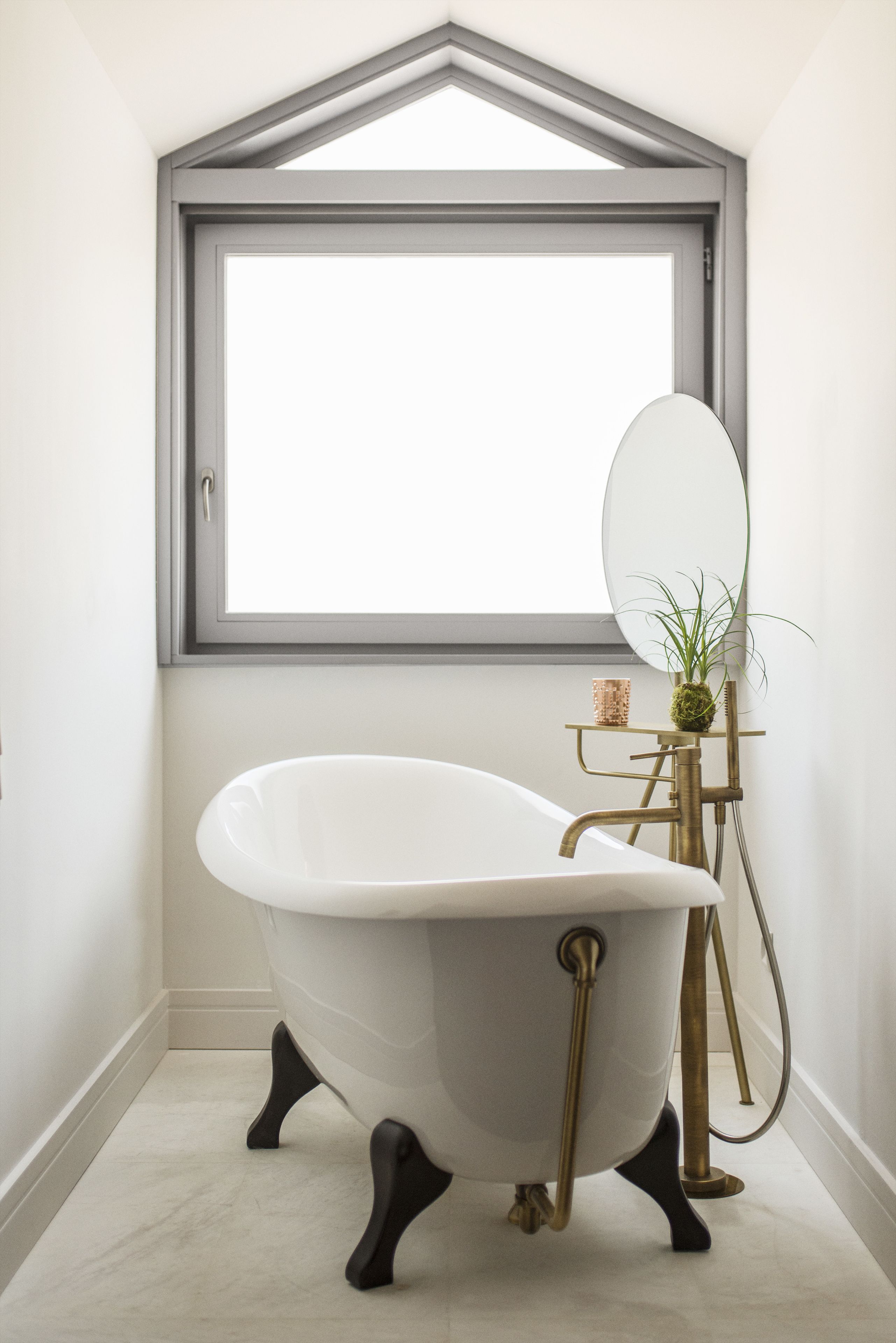 Un baño moderno con una bañera independiente, un espejo grande y una planta pequeña en una mesita.