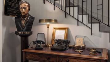 Un escritorio con un busto de José Rizal, una máquina de escribir antigua, una lámpara y un menú enmarcado.