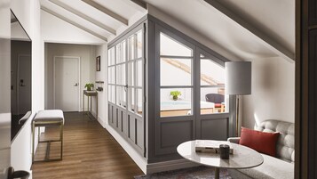 Un loft moderne avec un plafond haut, une grande verrière, un coin salon confortable agrémenté d’un coussin rouge et une petite table sur laquelle se trouvent un livre et une tasse.