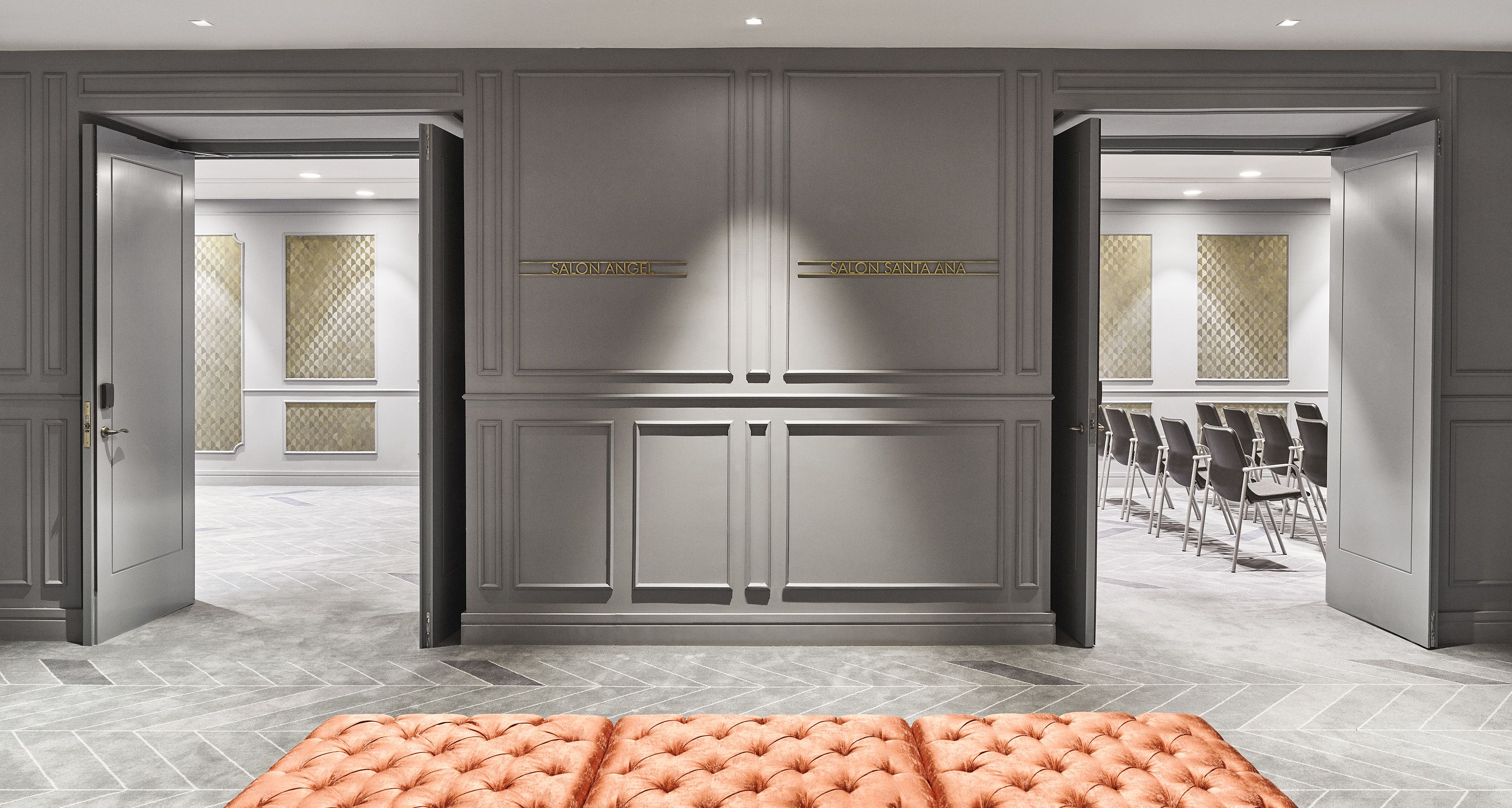 A hotel lobby with a grey tiled floor, a tufted orange sofa, and two doors labeled "SALON ANCH" and "SALON SANTA ANA".