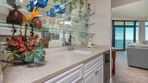 A kitchen with a granite countertop, white cabinetry, a large mirror, and a view of the ocean through large windows.