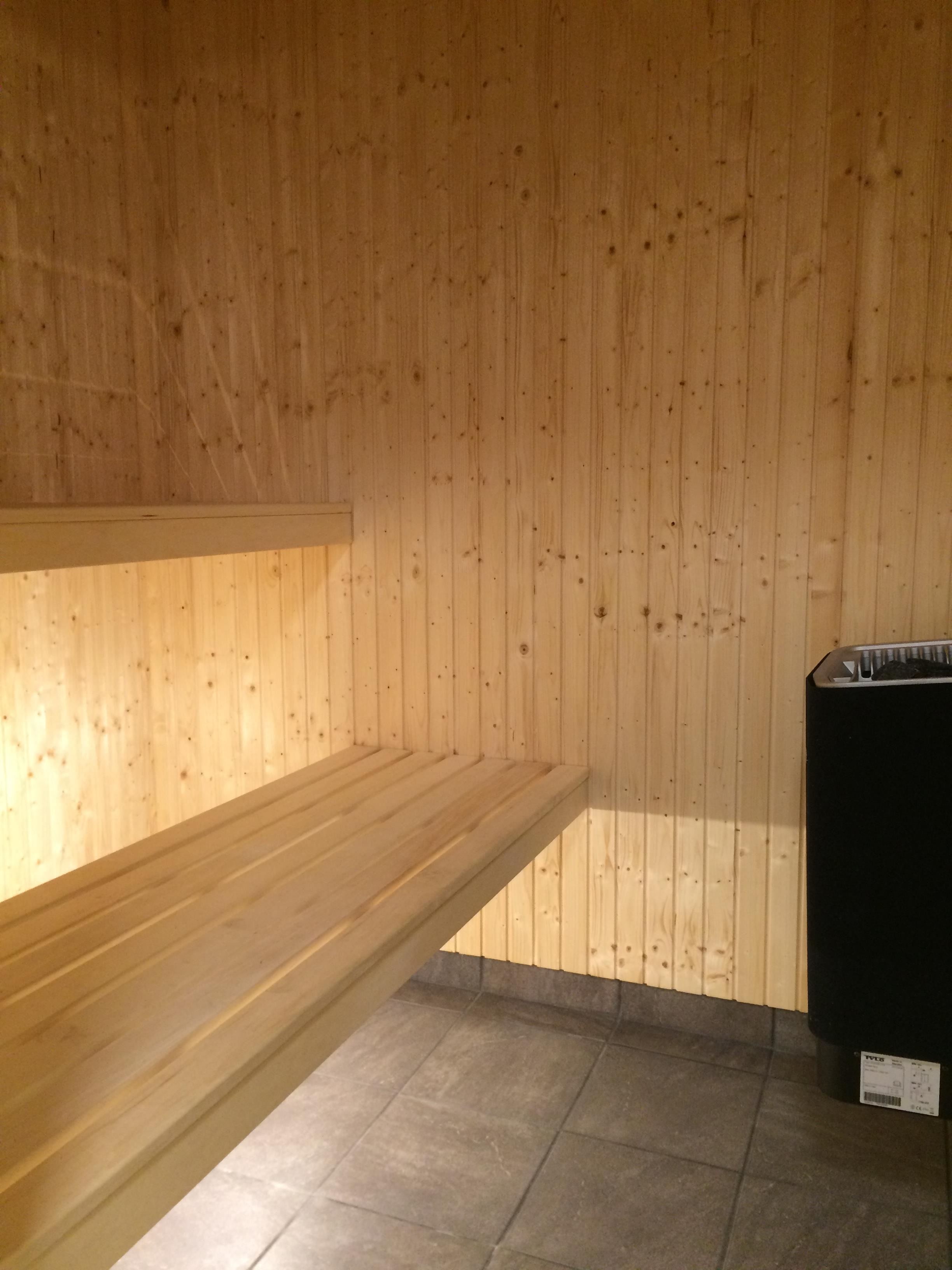 A room with wooden walls, a tiled floor, and a black trash bin.
