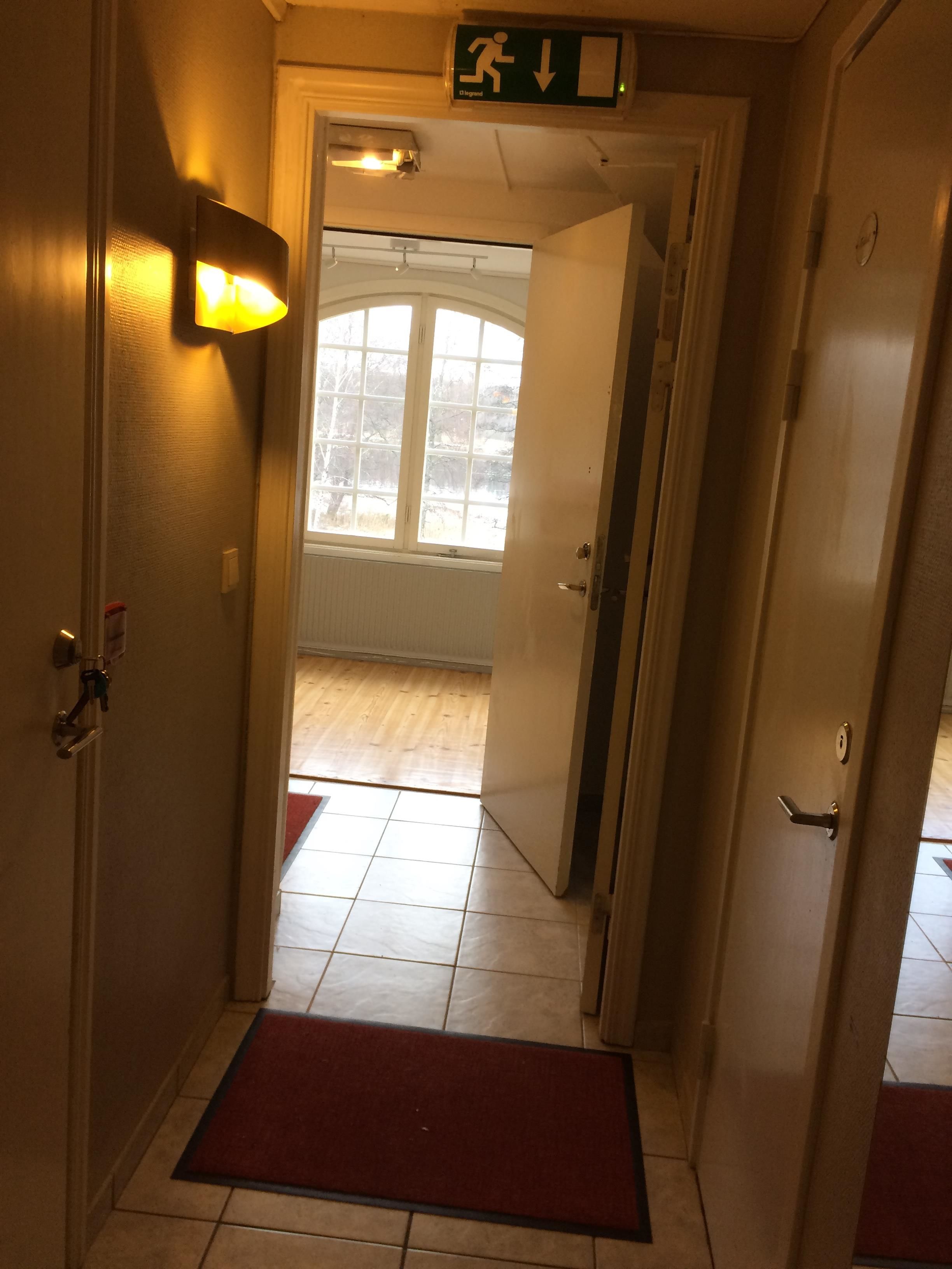 Um corredor com um tapete vermelho, uma porta com puxador e uma placa indicando a saída.