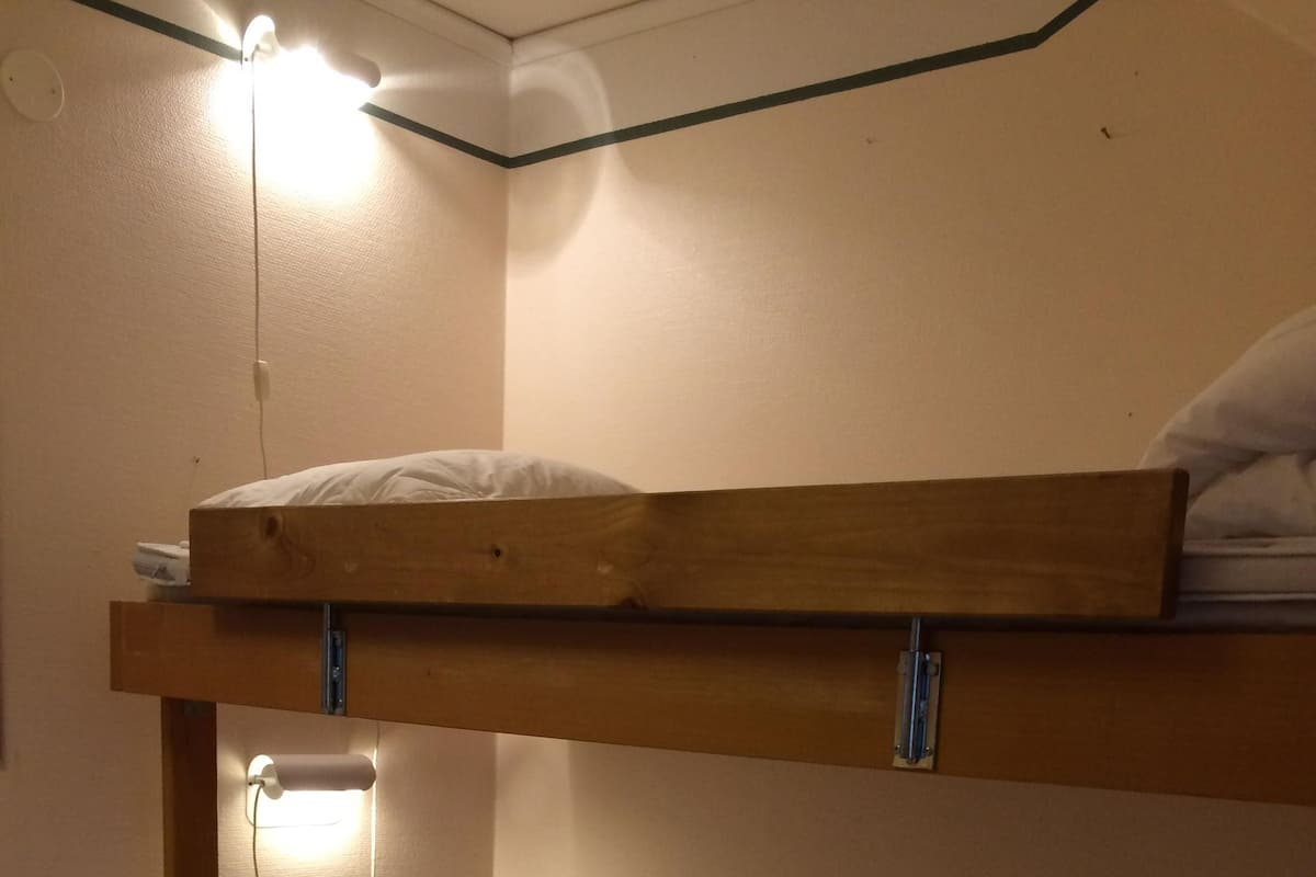 En køjeseng med en enkeltseng for neden, en lampe på væggen og en stikkontakt.