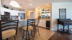 A kitchen with white cabinets, a microwave, a refrigerator, and a dishwasher. There are two bar stools with cushioned seats. - Phoenix West 3BR! LOW FLOOR! (Orange Beach)