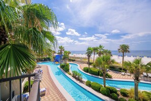 Área de piscina do resort com vista para a praia, cadeiras de sol e palmeiras.