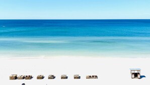 A beach with white sand and clear blue water. There are wooden lounge chairs and a small structure with a roof. - Relax in our spacious 1400sf 2/2 beach front condo with gorgeous sunset views! (Panama City Beach)