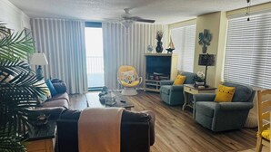 A living room with a sofa, armchairs, a TV, and a ceiling fan. - Relax in our spacious 1400sf 2/2 beach front condo with gorgeous sunset views! (Panama City Beach)