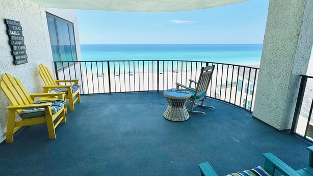 A balcony with yellow Adirondack chairs, a wicker table, and a view of the beach. - Relax in our spacious 1400sf 2/2 beach front condo with gorgeous sunset views! (Panama City Beach)