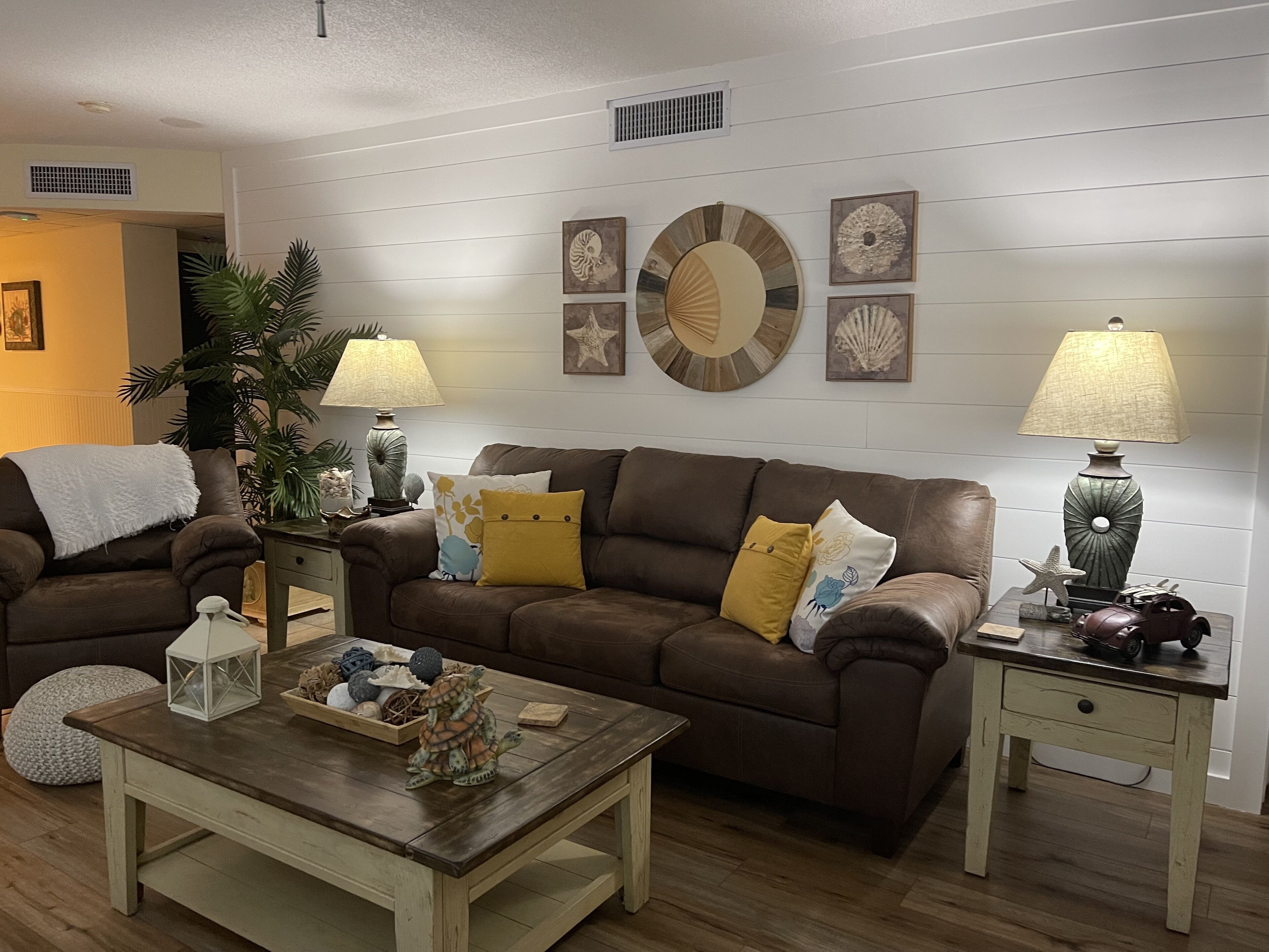 Una sala de estar con un sofá de cuero marrón, dos mesitas de noche con lámparas, una mesa de centro de madera y almohadones decorativos.