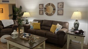 A living room with a brown leather sofa, two side tables with lamps, a wooden coffee table, and decorative pillows. - Relax in our spacious 1400sf 2/2 beach front condo with gorgeous sunset views! (Panama City Beach)
