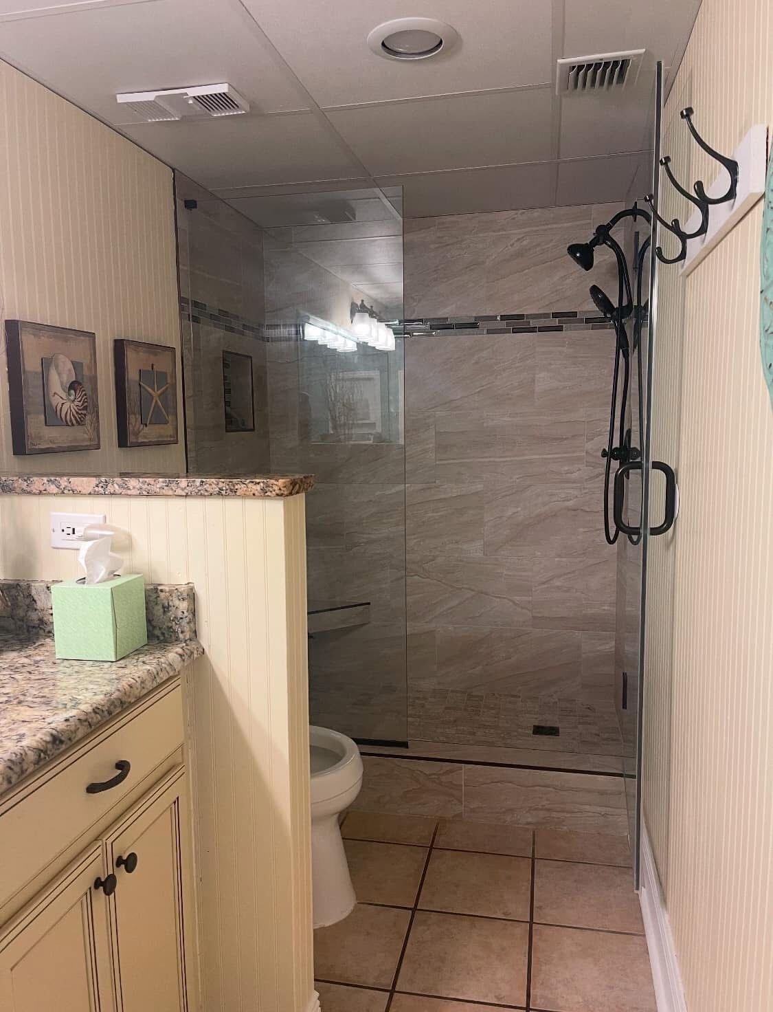 Un baño con ducha, inodoro y tocador con dispensador de toallas.
