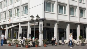 A hotel with a white facade, multiple windows, and outdoor seating with potted plants. - Hotel am Markt (Karlsruhe)
