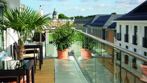 A balcony with potted plants, a glass railing, and a view of buildings in the background. - Hotel am Markt (Karlsruhe)
