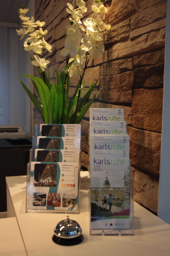 A reception area with a white orchid in a vase, a stack of brochures, and a black bell on a white table against a stone wall backdrop.