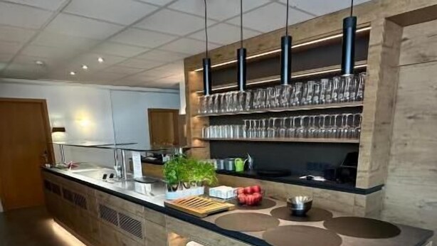 A modern kitchen with a central island, pendant lights, and a glass display of wine glasses. - Hotel am Markt (Karlsruhe)