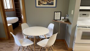 A dining area with a round table and four chairs, a kitchen with a stove, and a framed artwork on the wall.