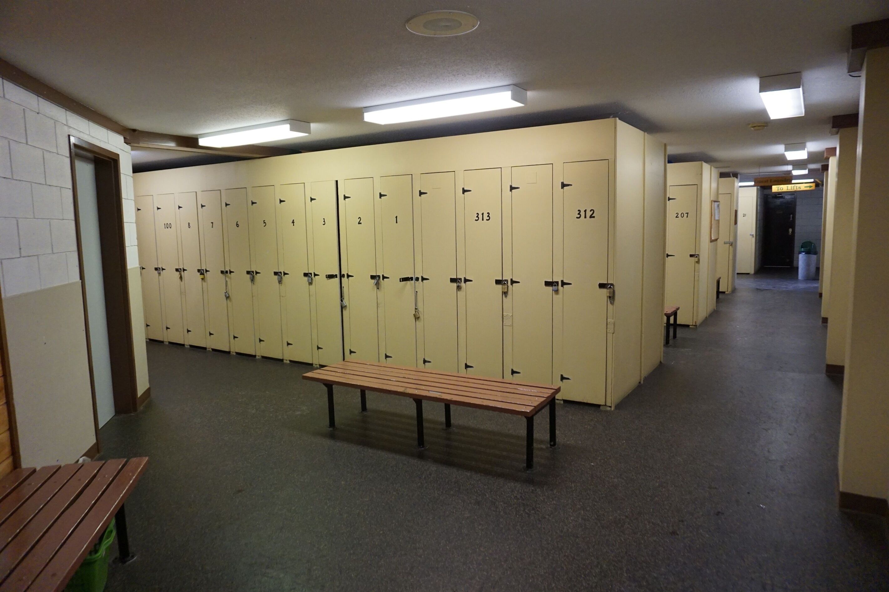 A locker room with numbered lockers, a bench, and a trash bin.