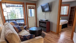 A living room with a sofa, ottoman, and a flat-screen TV mounted on the wall.