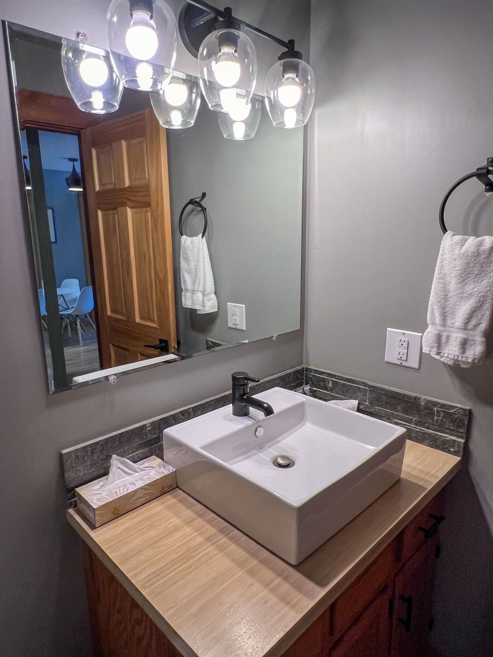 A bathroom with a large mirror, a white sink, and a wooden vanity.