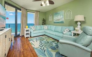 A living room with a sectional sofa, a small side table, a floor lamp, and a view of the ocean through large windows.