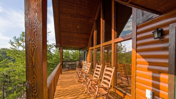 Eine Holzterrasse mit Schaukelstühlen und einem Tisch, mit Blick auf einen bewaldeten Bereich.