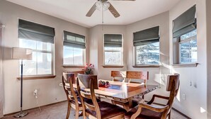 Un comedor con una mesa y sillas de madera, un ventilador de techo y ventanas con persianas.