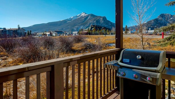 Una terraza de madera con una parrilla Weber Spirit, con vistas a un paisaje montañoso con casas y vegetación escasa.