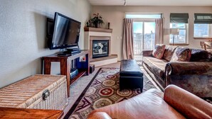 Una sala de estar con televisión, chimenea, sofá y vistas al exterior.