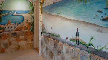 Um mural retratando uma cena costeira com um muro de pedra e uma garrafa de vinho.