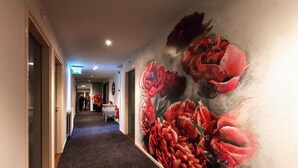Un couloir orné d’une grande fresque murale représentant des motifs floraux, doté d’un sol recouvert de moquette et terminé par une porte.