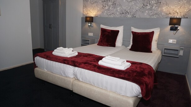 A double bed with white linens and a red velvet throw, two wall-mounted lamps, and a floral-patterned wall. - Hotel Hartlief (Buinen)