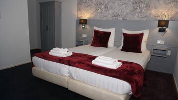 A double bed with white linens and a red velvet throw, two wall-mounted lamps, and a floral-patterned wall.